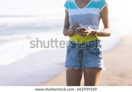 Hipster girl hold smart phone gadget in sand coastline, mock up of blank screen. Traveler using in female hand mobile on background seascape horizon. Tourist look on blue sun ocean, lifestyle 