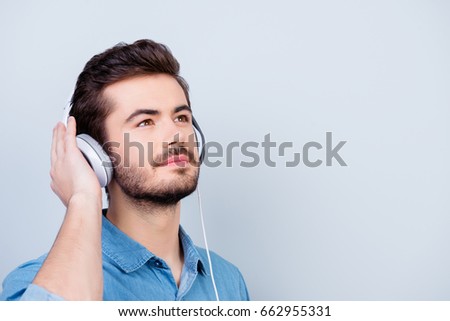 Dreamy young cute guy is looking up imagining something nice. He is listening to the music in white big earphones on pure background