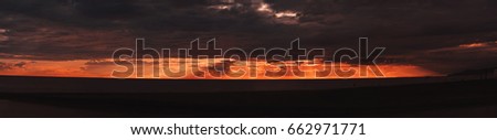 Wide panorama of stunning sunset on Black Sea during summertime with dramatic evening sky and clouds, dark pebble coastline with silhouettes; Sochi, Russia