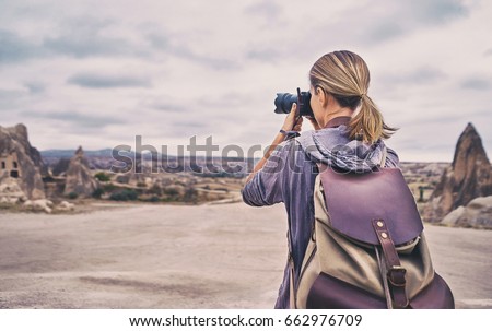 Traveling and photography. Young woman with camera and backpack taking picture at Cappadocia, Turkey.