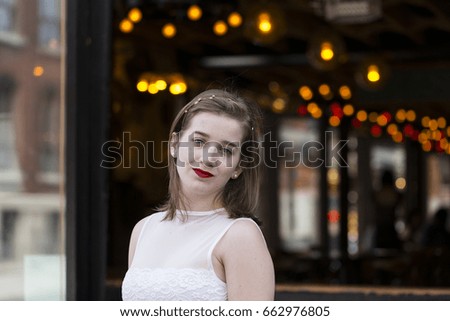 Medium shot of beautiful young woman in white top and head band with head tilted and lights in soft focus background