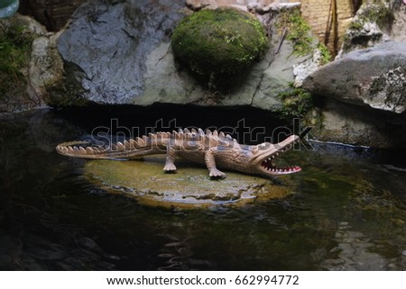 The replica of crocodile on the rock at the pond with water background.