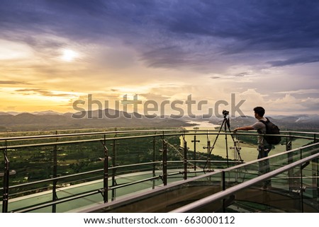 Photographer taking photos of beautiful sunset behind the city and river on sky walk on the mountain.