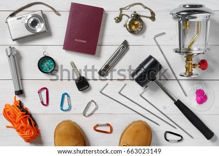 travel equipment for holiday passport, boots, lantern, wick, knife, camera, tripod, compass, clock, hammer, car key, carabiner, anchor and tent rope on white vintage wood floor or table top view
