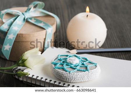 Gift box with star ribbon, blank note book, crochet paperweight on dark rustic table. Greeting card with heart and lit candle, toned image