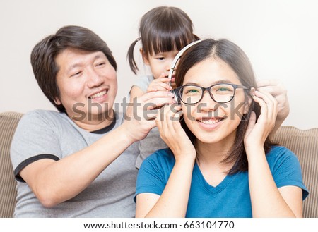 Asian parents and baby girl in sofa using tablet and headphones