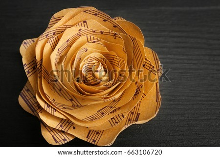 Beautiful rose made of music notes on wooden table closeup