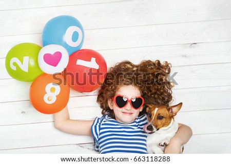 Cute girl embracing her puppy dog and holding rainbow balloons. New Years 2018, Christmas holiday concept. Lying on the wooden floor with high top view.