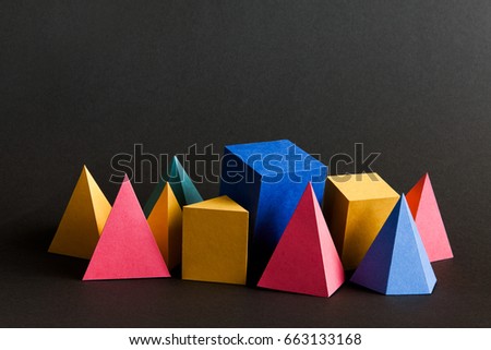 Colorful abstract solid figures composition. Three-dimensional prism pyramid rectangular cube geometric objects on black paper background. Red blue yellow green colored, soft focus photo
