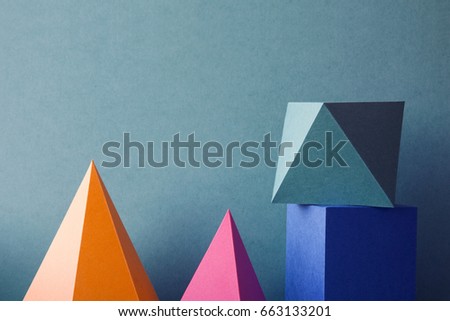 Pyramid prism rectangular cube arranged on green paper. Colorful abstract geometric background with three-dimensional solid figures. Yellow blue pink malachite colored geometrical shapes. Soft focus.