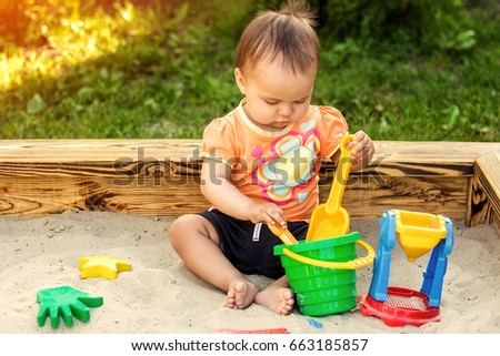 Happy little girl playing in a sandbox on the playground. Summertime children activities