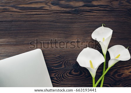 flat lay white calla flowers and a laptop on a wooden background, top view.