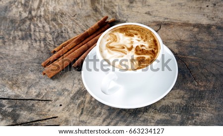 Hot cappuccino or latte art. A cup of coffee on the wooden table with dark roasted beans. Morning breakfast with coffee. Dragon with wings and fire shape created by pouring steamed milk.