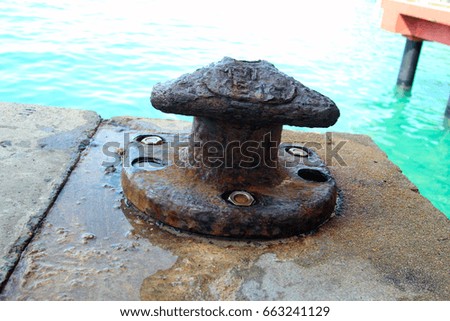 A bollard on a jetty over a blue sea water background