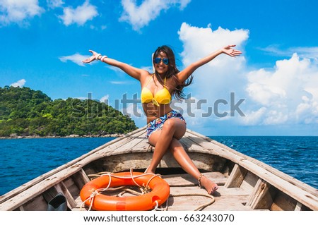 Asian woman in bikini relaxing on wooden boat her arms open feeling freedom, Andaman sea, Phangnga, Thailand