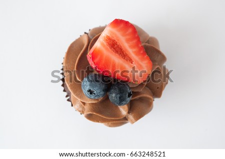 Chocolate cupcake with whipped chocolate cream, decorated fresh strawberry, blueberry on white background. Picture for a menu or a confectionery catalog. Top view.