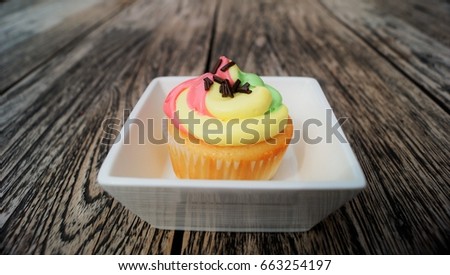 Rainbow cupcake. Homemade decorated vanilla cupcake with colorful rainbow pastel frosting on vintage wood table background