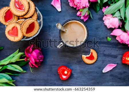 The concept of morning coffee in a romantic style on the black wooden background. Peonies flowers and petals, cookies, heart candles, mug with coffee . Valentine's love day. Top view