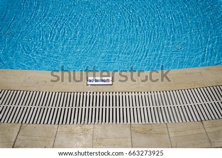 Outdoor swimming pool with no diving sign.
Open air poolside with clear blue water on a sunny day.