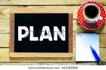 Plan handwritten on blackboard with cup of coffee, notepad and pen on wooden table background