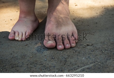 the feet of a little boy and a man on the sand