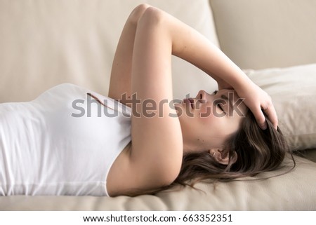 Woman lying on sofa having headache. Stressed girl suffering of fatigue, migraine, trying to cope with nervous tension, worries because of problems, unwanted pregnancy, negative thoughts and emotions Royalty-Free Stock Photo #663352351