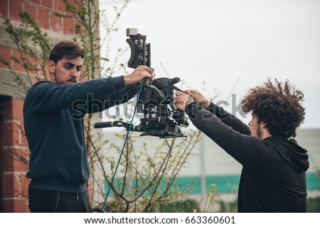 Behind the scene. Cameraman and assistant shooting the film scene with camera on outdoor location