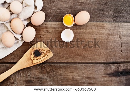 Farm fresh organic brown chicken eggs from free range chickens with an old olive wood antique spatula over a rustic wooden background. One egg cracked open showing yolk.