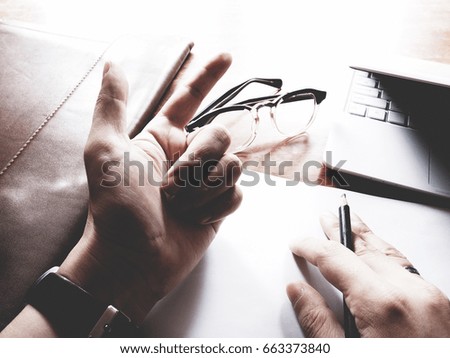 The picture of hands working action on wooden table, consist of laptop, paper, pencil, watch, glasses, soft tone color