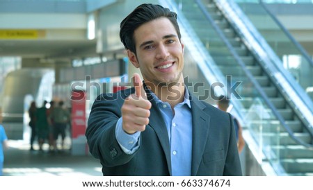 Portrait of a young handsome businessman in suit, at the station, leading business affairs, smiling, background with an escalator. Concept: new business, business relationships, career growth, success