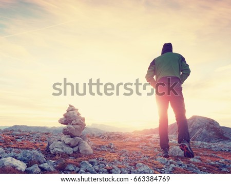 Tourist guide at stocked stones on Alps peak. Strong hiker enjoy sunset in   Alpine mountain. Alone man on few days trek