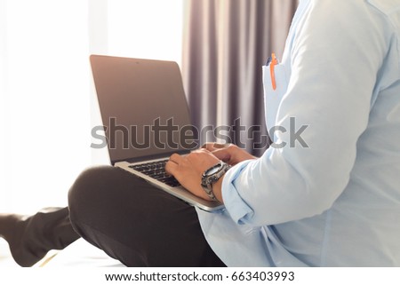Man's hands using laptop with blank screen on bed in home interior.