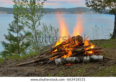 Big night bonfire on the riverbank in the forest clearing, flames, sparks and fireplace.