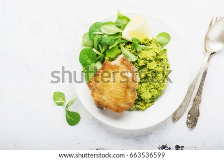 Easy healthy lunch: chicken thigh with mashed green peas and corn salad on a light background. Top view.