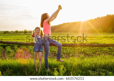 Children in the background of nature play with a smartphone. The picture is taken against the sunset.