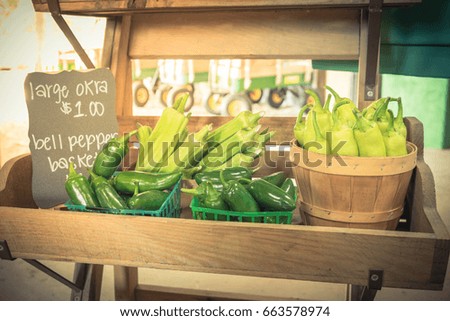Close-up full baskets of large okra (lady fingers) and bell peppers with price tags on display at local farm store in Texas, US. Fresh picked organic produce for sale, steel stake wagons in background