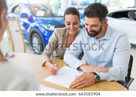 Young couple with car dealer in auto salon Royalty-Free Stock Photo #663585904