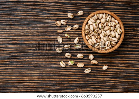 Pistachiosin brown bowl on textured wooden background, top view.