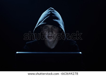 A hacker in a hood, a hacker breaks into networks, a hacker on a dark background.