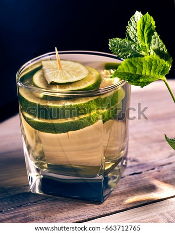 Non alcohol drink. On wooden boards is glass with green transparent drink. Soft drink with lime and mint leaf on black background. Country life.
