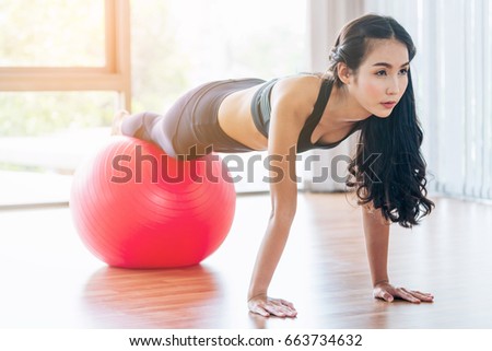 Woman doing exercises with red fit ball in fitness gym class. Fitness ball helps women get a toned, tight stomach and strong core. Concept of healthy lifestyle for women fitness.