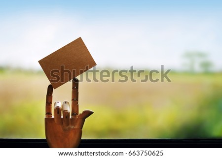 Blank craft paper card for mockup on Wooden mannequin hand with three finger sign, Glass Window and blurred nature landscape as background