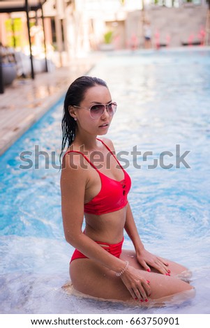 Spending hot summer day poolside. Beautiful young woman in red bikini relaxing by the pool.