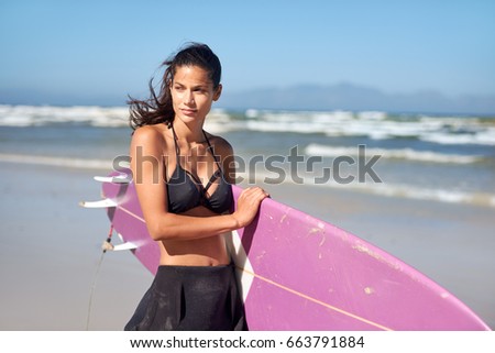 Fit athletic surfer girl holding surf board on the beach, sunny day blue skies waves in background