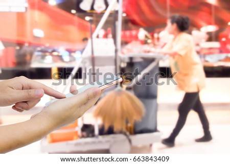 Man use mobile phone, blurred image of the cleaning staff in the mall as background.(Building cleaning service is just a phone call away.)