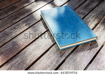 An old blue book on top of a wooden table. This image can be used to represent casual reading. 