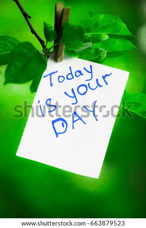 Motivating phrase today is your day. On a green background on a branch is a white paper with a motivating phrase