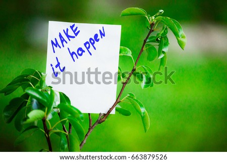 Motivating phrase make it happen. On a green background on a branch is a white paper with a motivating phrase