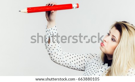 Confused sad blonde student girl or young female teacher holding big red pencil, drawing. Studio shot on grey