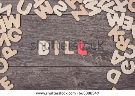 Word bill made with wooden letters next to a pile of other letters over the wooden board surface composition